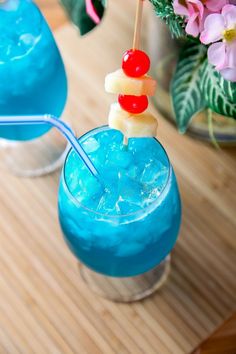 two glasses filled with blue liquid and pineapple on the top, next to pink flowers