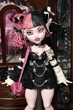 a doll is standing in front of a dresser with pink hair and black clothes on