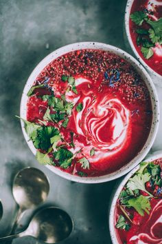 two bowls filled with red soup and garnished with cilantro, parsley and mint