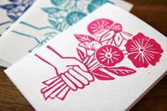 three cards with flowers on them sitting on top of a wooden table next to each other