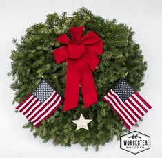 a wreath with two american flags hanging from it's sides and a bow on top