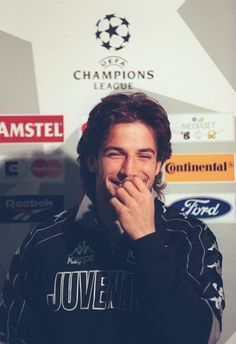 a man with his hand to his mouth in front of a wall covered with signs