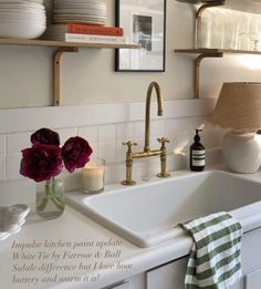 a white kitchen sink sitting under a window next to a shelf filled with plates and bowls