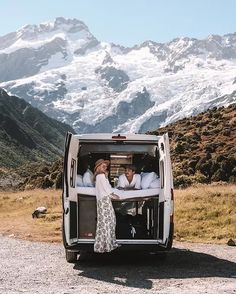 the back end of a van with two people in it and mountains in the background