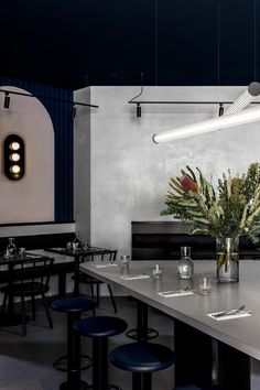 an empty restaurant with blue stools and plants in vases on the counter top