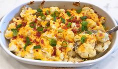 a casserole dish with cauliflower, green onions and bacon in it