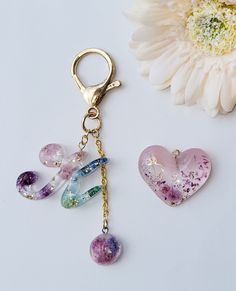 two heart shaped key chains with charms attached to them next to a flower and a daisy