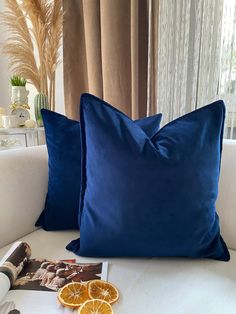 two blue pillows sitting on top of a white couch next to an orange slice and magazine