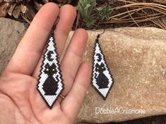 a hand holding two black and white beaded earrings