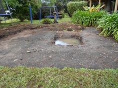 an open hole in the ground with trees and bushes around it, next to a swing set