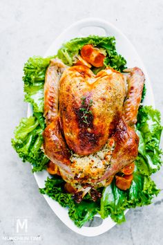 a whole chicken on top of lettuce and carrots in a white plate