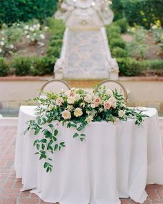 a table with flowers and greenery on it in the middle of a garden area