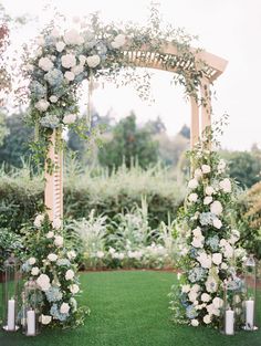 an outdoor wedding ceremony setup with white flowers and greenery on the grass, surrounded by candles