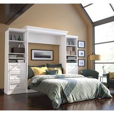 a white bed sitting under a window next to a wooden floor