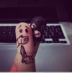 two fingers with faces drawn on them next to a laptop