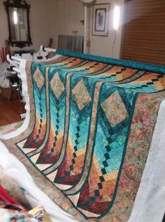 several quilts are laid out on a table in a room with chairs and other items