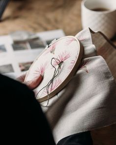 a person holding a piece of fabric with embroidery on it and a cup of coffee in the background