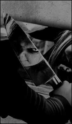 black and white photograph of a person holding a large knife in their left hand, with the reflection of a woman's face on it