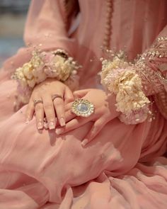 a close up of a person in a pink dress with flowers on her hand and an engagement ring