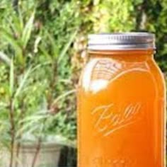 an orange mason jar sitting on top of a wooden table next to some potted plants