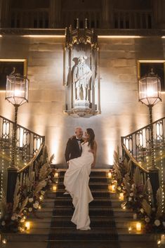 a bride and groom are standing on the stairs in front of an ornate staircase with candles