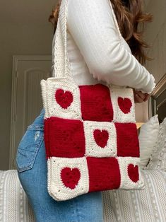 a woman holding a red and white crocheted bag with hearts on it's sides