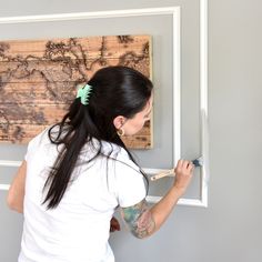 a woman is painting a map on the wall with paint rollers in her hand