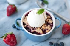 blueberry cobbler with ice cream on top and strawberries around the bowl, ready to be eaten