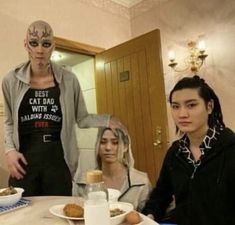 three people sitting at a table with plates of food in front of them and one woman standing next to her