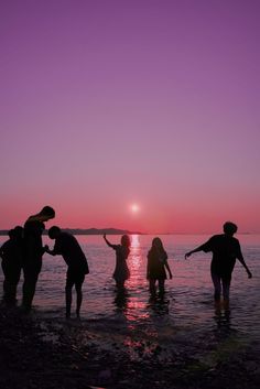 several people standing in the water at sunset