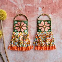 two pairs of beaded earrings sitting on top of a pink surface next to a flower