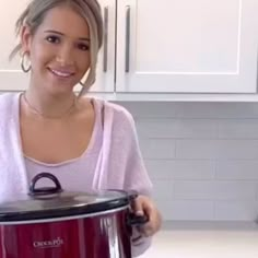 a woman standing in front of a red crock pot with the lid open and smiling