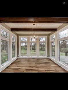 an empty room with large windows and wood flooring on the walls, along with a chandelier