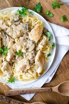 a white plate topped with pasta covered in sauce and mushrooms next to wooden spoons