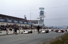 a group of people watching race cars go down the road in front of spectators at an event