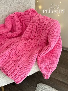 a pink knitted blanket sitting on top of a white chair next to a rug