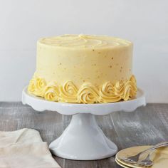 a white cake with yellow frosting sitting on top of a table next to a plate