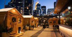 a row of wooden buildings sitting next to each other on top of a sidewalk in front of tall buildings