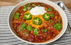 a bowl of chili with sour cream and jalapenos in it on a striped napkin