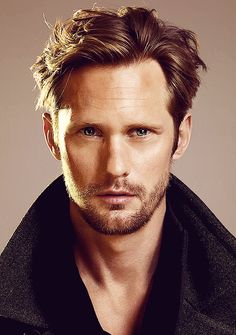 a close up of a person wearing a black shirt and jacket with his hair blowing in the wind