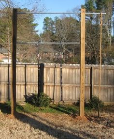 a fenced in yard with some trees and bushes next to it, along with a tall wooden pole