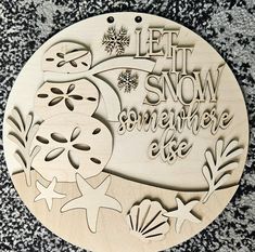 a wooden plaque that says let it snow somewhere elsee on the ground with sea shells and starfish