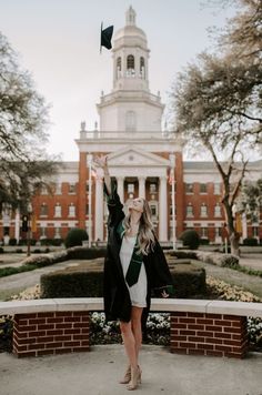 a woman is standing in front of a building and throwing her graduation cap into the air