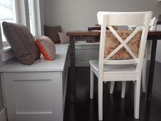 a white chair sitting in front of a window next to a table with two pillows on it