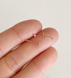 a hand holding a pair of tiny gold nose studs with small diamonds on them