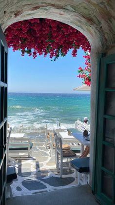 an open door leading to the beach with red flowers on it and water in the background