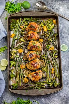 chicken and asparagus on a baking sheet with lemons, parsley and lime wedges