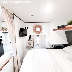 a white bed sitting in a bedroom next to a tv on top of a wooden shelf