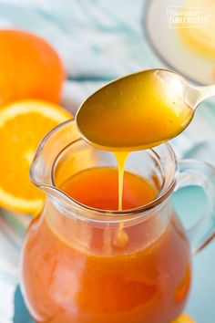 a spoon pouring orange juice into a glass pitcher