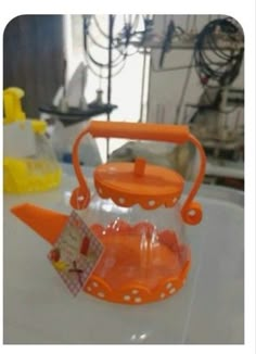 an orange teapot with a plastic handle on it's side sitting on top of a table